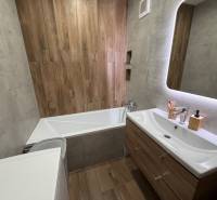 Bathroom with a mirror, bathtub, sink, and floor with a wooden decor in a 4-room apartment.