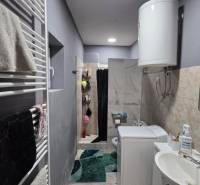 A bathroom in a family house with a sink, washing machine, boiler, and shower.