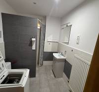 A bathroom in a family house with a shower, washing machine, and sink, furnished with tiles.