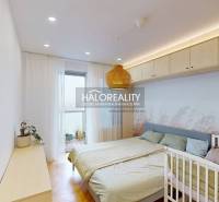 A bright bedroom with wood-patterned flooring, a double bed, and a baby crib in a three-room apartment.