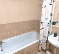 A bathroom in a 2-room apartment with a bathtub and tiles in neutral shades.