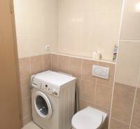 Bathroom in a 2-room apartment with light tiles, a washing machine, and a wall-hung toilet.