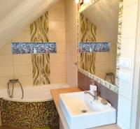 Bathroom in a family house with a bathtub, sink, mirror, and mosaic decoration.