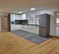 A kitchen in a family house with white cabinets, gray tiles, and a wooden decor floor.