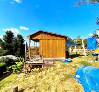 A wooden cabin in Partizánske surrounded by nature, with a grassy plot and outdoor seating.