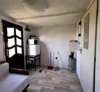 A room in a cottage with a sofa, fridge, microwave, and simple furniture.