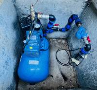 In a concrete pit, there is a blue pressure water pump system with piping.