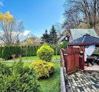 A garden by the cottage in Partizánske with a gazebo, trimmed bushes, and trees.