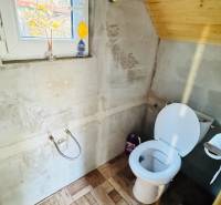 A toilet in a wooden cabin, with a wooden decor floor and a window.