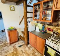 A kitchen in a cabin with wooden decor, stairs, appliances, and furniture with a stone wall.