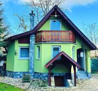 A cottage in Partizánske with a wooden balcony, surrounded by greenery and a paved courtyard.
