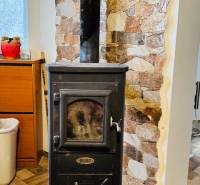 Wood-burning stove with a chimney, stone wall, wooden decor flooring in a cabin.