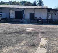 On Železničná Street, there are warehouses and halls, a space with parking and cars.