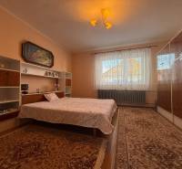 Bedroom with carpets, bed, shelves, and a painting in a family house.
