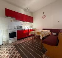 A kitchen in a family house with a red kitchen unit, a sofa, a dining table, and tiles.