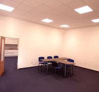 An office with blue chairs and tables, white wall, open door to a small kitchenette.