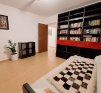 A room in a 4-room apartment with shelves full of books and a floor with a wooden decor.