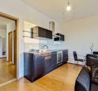 A kitchen in a studio apartment with black furniture and a wooden decor floor.