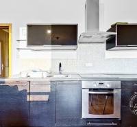 A kitchen in a studio apartment with black kitchen cabinets and a wooden decor floor.