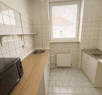 A kitchen space with white tiles, a microwave, and a wood-patterned floor.