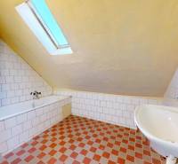 A bathroom in a family house with a bathtub, sink, and sloped ceiling.