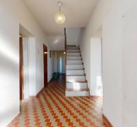 A hallway in a family house with ceramic tiles and a staircase, softly lit by a lamp.