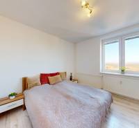 A bright bedroom with wood-patterned flooring and a large window in a three-room apartment.
