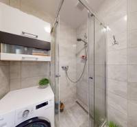 A bathroom in a 3-room apartment with a washing machine, shower, and storage cabinets.