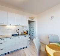 A kitchen in a 3-room apartment with a wood-patterned floor, a dining table, and white cabinets.