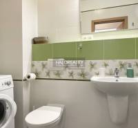 Bathroom in a studio apartment with a washing machine, sink, and green tiles.