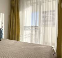 Bright bedroom in a one-room apartment with a large window and curtains.