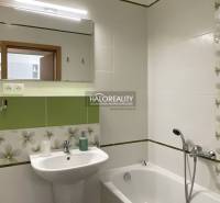 A bathroom with green and white tiles, a bathtub, and a sink, suitable for a studio apartment.
