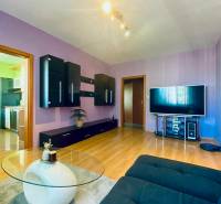 Living room of a three-room apartment with purple walls, dark furniture, and a TV on a wooden-decor floor.