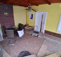 The terrace of the family house with tiles and seating furniture. In the alcove, there is a table and a clock.