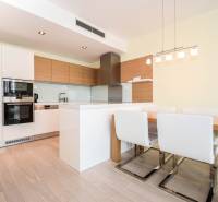 A kitchen with white cabinets, a dining table, and a wooden decor floor in a 3-room apartment.
