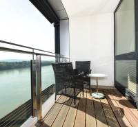 Balcony with a view of the river, two chairs, a table, wooden floor decor.