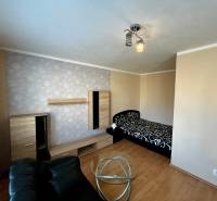 A room in a one-room apartment with a bed, a black armchair, and a floor with a wood decor.