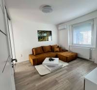 A bright living room in a two-room apartment with a brown sofa and a table on a floor with a wooden decor.