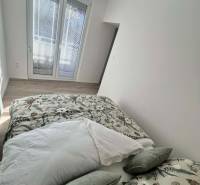 Bright bedroom in a two-room apartment with decorative pillows and a wooden-patterned floor.