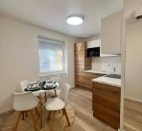 A kitchen in a 2-room apartment with a table, chairs, and a wooden decor floor.