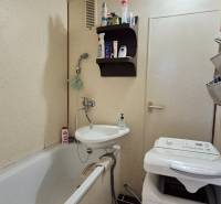 Bathroom in a 2-room apartment with a bathtub, sink, and washing machine, minimalist accessories.