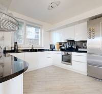 A kitchen in a 5 or more room apartment with glossy white cabinets and a wood-patterned floor.