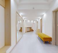 A hallway in a 5 or more room apartment with white walls and a yellow bench.