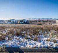 Snow-covered residential plots in Mlynica with sunny weather and visible houses in the background.