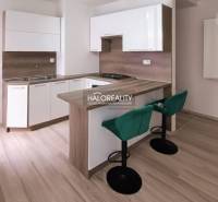 A kitchen in a 2-room apartment with a bar counter, green chairs, and a wooden decor floor.