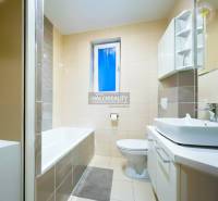 A bathroom with a bathtub and a sink in a 2-room apartment, featuring light-colored tiles.
