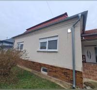 A family house in Hurbanovo with a light facade and a red roof, surrounded by bushes.