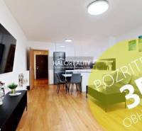 Living room in a two-room apartment with a wooden decor floor, dining area, and a TV on the wall.