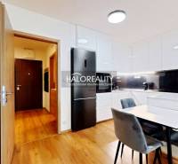 A kitchen in a 2-room apartment with a dining table, built-in kitchen unit, and a floor with a wood decor.