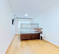 A bright bedroom with a bed, a nightstand, and a TV in a two-room apartment, with a wood-patterned floor.